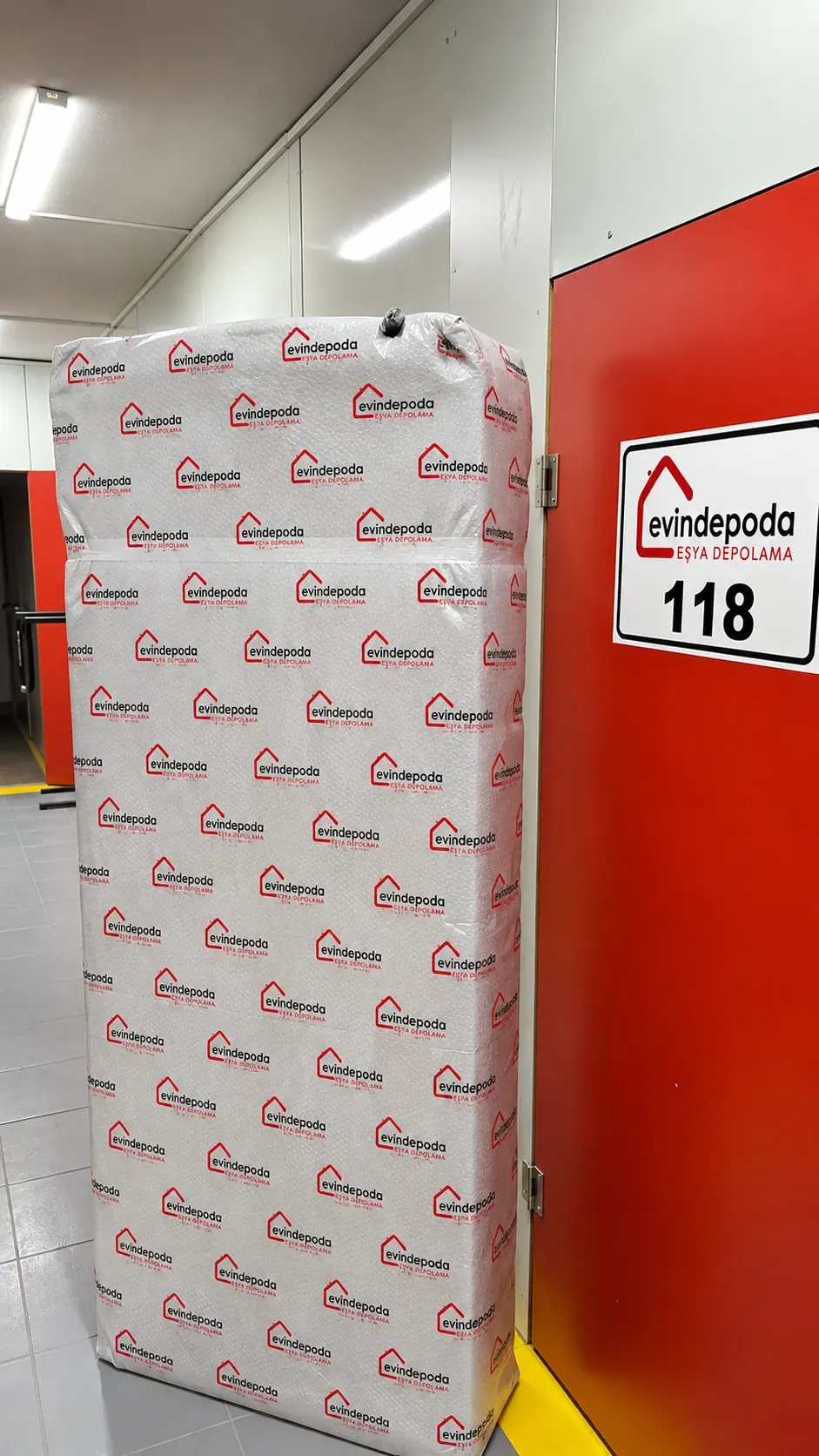 Logolu sargı malzemesiyle paketlenmiş eşya, 118 numaralı depo odasının önünde