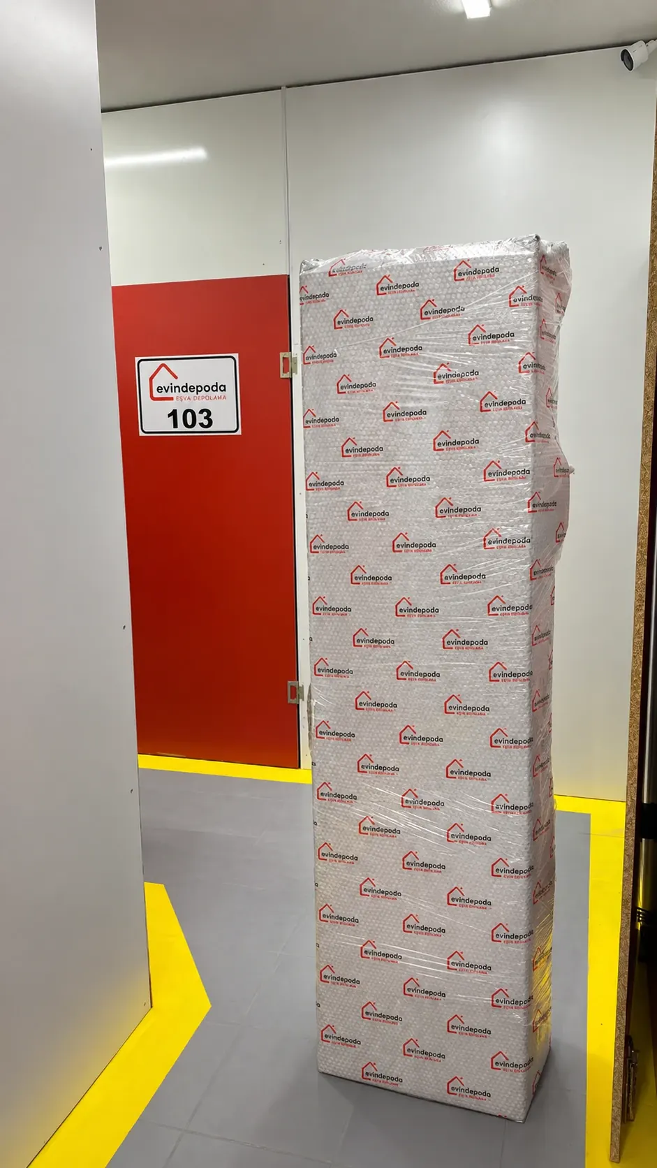 Logolu sargı malzemesiyle paketlenmiş uzun eşya, 103 numaralı depo odasının önünde